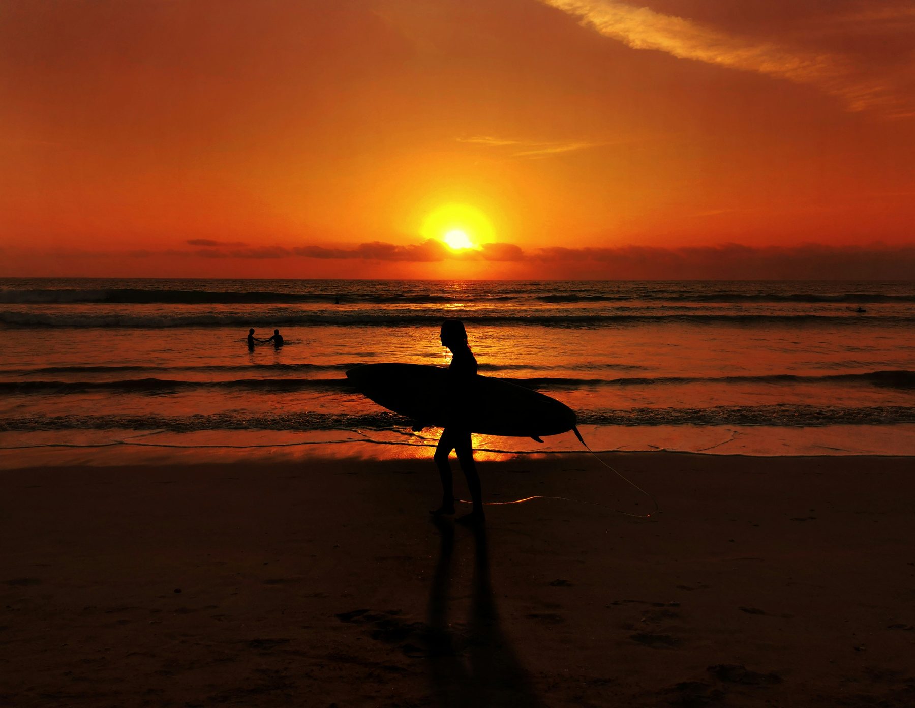 A woman carrying a surfboard on a Bali beach at sunset